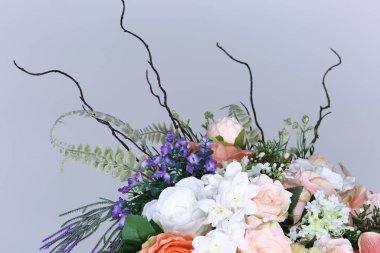 Roma cam vazosunun üzerinde bir buket pembe beyaz çiçek var. Suni, stüdyo gri arka planı aydınlatıyor.