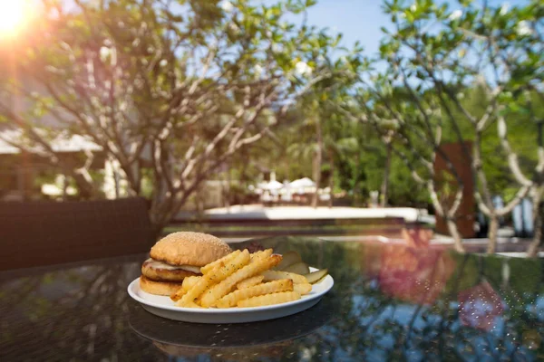 Chicken Beef Beacon Ham Cheese Burger with fried potato chip, Fusion food stylish arrange on glass table along ocean mangrove tree Island, empty copy space for text logo Yummy