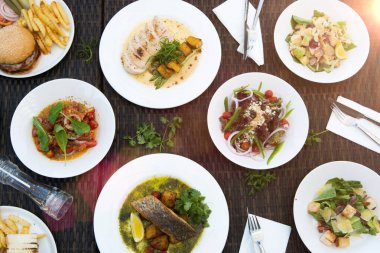 Karışık deniz ürünleri, spagetti, kulüp sandviçi, burger, salata, sıcak baharatlı yiyecekler tropikal okyanus atmosferinde masada, arkadaşlarla akşam yemeği.