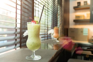Yüksek bardakta yeşil meyve suyu, buzlu saman tübü ve müşteri için süsleme süsü, öğle yemeği masası pencere kenarı koltuğu için diyet yapmak için taze meyve suyu.