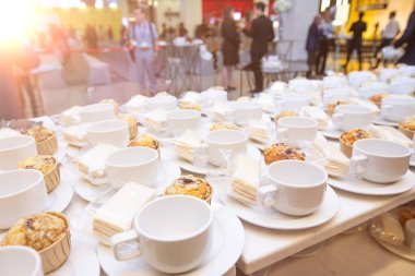 Tabağında abur cubur olan bir grup boş kahve fincanı. Açık büfede sıcak çay ya da kahve servisi için bir sürü beyaz fincan ve bulanık insanlar üzerinde seminer etkinliği kalabalık arka planlar, sığ noktalar veya daha fazla bulanıklık