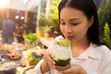Güzel, yetişkin, çalışan bir kadın buzlu sütlü yeşil çay içer ve dudaklarında köpükle gülümser. Bir sürü yemek tabağı ve restorandaki insanlar, seçici odak bulanıklığı.