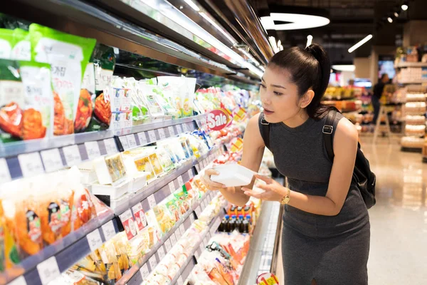Mother Asian Working woman select pick up healthy nutrition food, yogurt milk from supermarket shelf rack after work. Concept decision Making choice select best thing for kid children family