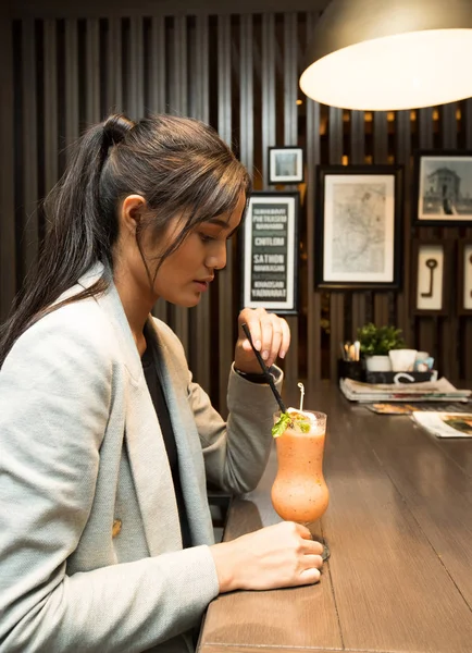 A beautiful working woman side rear view having drink fruit smoothies Juice and sit looking at bar in a cafe, creative lady thinks about work and refreshment her brain