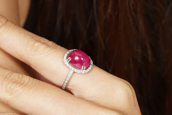 红指甲和棕色头发背景的女人手上的红宝石钻石戒指 — 图库照片