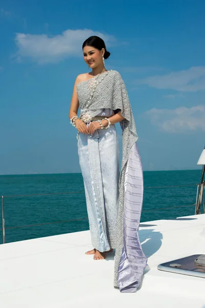 Asian Woman in Blue gray Thai Traditional Costume with jewelry accessories get Winds on Luxury Yacht boat ship in Green Ocean nice sky, Lady relaxing on cruise wearing old formal dress