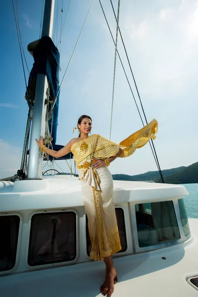 Asian Woman in Gold Yellow Thai Traditional Costume with jewelry accessories get Winds on Luxury Yacht boat ship in Green Ocean nice sky, Lady relaxing on cruise wearing old formal dress