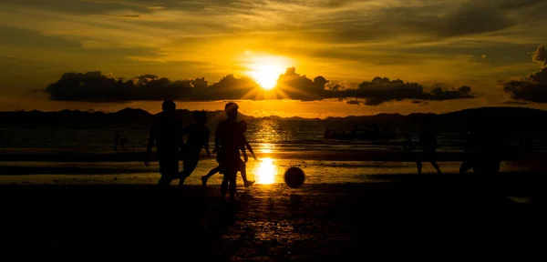 Back Light sunset silhouettes of unrecognizable beach football people playing, Local villager play soccer with foreigners team during sun down along tropical beach with cheerful