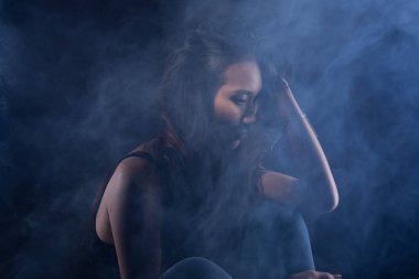 Beyaz dumanlı bronz tenli Asyalı kadın koyu arkaplanda yoğun kabarık tüylü sisli düz saçlı, soyut düşük pozlu kontrast, metin logosu için kopya alanı, kırık kalpli yalnız kız ağlayabilir.