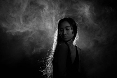 Beyaz dumanlı bronz tenli Asyalı kadın koyu arkaplanda yoğun kabarık tüylü sisli düz saçlı, soyut düşük pozlu kontrast, metin logosu için kopya alanı, kırık kalpli yalnız kız ağlayabilir.