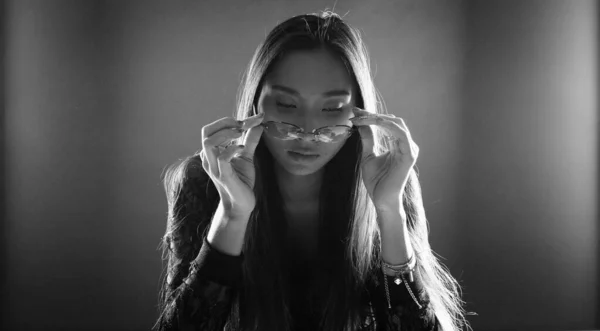 Black White monochrome with Noise Grain, Portrait of Asian Woman long straight hair try to wear new glasses on her face and look so fashion stunning with dramatic light on rear side