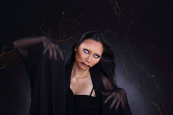 Witchcraft Asian woman in scary Witch ghost story look, white eyes cut mouth blood wound black long hair, studio lighting dark background wood branch stick