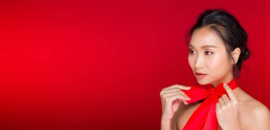 Asyalı siyah saçlı, bronz tenli, güçlü kırmızı dudaklı bir kadının moda portresi. Stüdyo kırmızımsı arka plan fotokopi alanı, kız kravatları kırmızı kurdele ve rüzgar esintisi, seçici odaklanma.