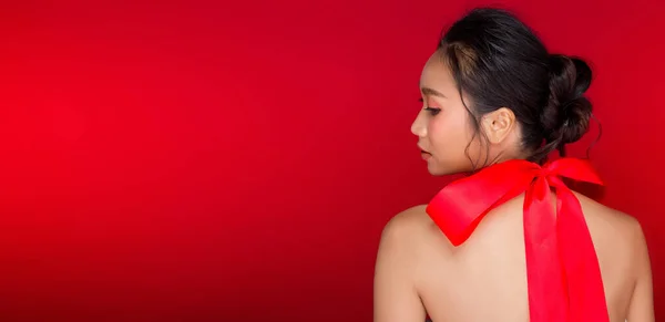 Fashion portrait of Asian Black hair tanned skin woman with strong color red lips, studio lighting red reddish background copy space, girl ties bow red ribbon and wind blow, selective focus