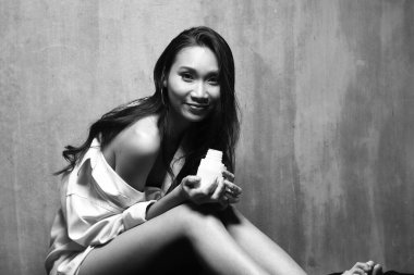 Güzel Asyalı Uzun düz siyah saçlı beyaz erkek gömlekli kadın, yüksek seksi moda makyaj yüzü, konsept uyan sabah yatak odası tarzında süt içen seksi kadın.