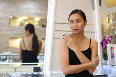 Yakından çekilmiş elmas yüzük, kolye, blacelet, siyah elbiseli, siyah tenli, zarif siyah saçlı, makyajlı ve siyah tırnaklı bir kız..