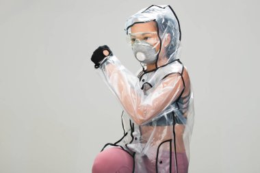 Asyalı bronz tenli spor kadın kol esnetme egzersizi spor sutyen eldiven şeffaf yağmurluk maske güvenlik gözlükleri stüdyo aydınlatma gri arka plan, gelecekteki kirlilik kavramı