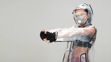Asyalı bronz tenli spor kadın kol esnetme egzersizi spor sutyen eldiven şeffaf yağmurluk maske güvenlik gözlükleri stüdyo aydınlatma gri arka plan, gelecekteki kirlilik kavramı