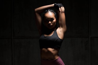 Asyalı bronz tenli spor kadın kollarını esneterek boks yapıyor. Arka planda, stüdyo aydınlatma gradyanı gri üst gölge düşük pozlama fotokopi alanı, konsept kadın 6 paket spor yapabilir.