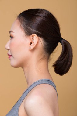 Kuaför makyajı yaptıktan sonra Asyalı kadın. Rötuş yok, sivilceli yeni bir yüz, dudaklar, gözler, yanak, hoş pürüzsüz bir cilt. Stüdyo ışıkları sarı bej hardal arkaplan, arka görünüm