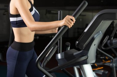 İnce Asyalı Fitness kadını siyah saçlı spor sutyen, Fit Gym 'de tırmanma makinesinin eliptik haçı üzerinde ısınıyor. Kavramsal kadın sporcu olabilir. Sağlıklı, yarı vücut, yüzsüz.