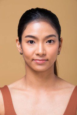 Kuaför makyajı yaptıktan sonra Asyalı kadın. Rötuş yok, sivilceli yeni bir yüz, dudaklar, gözler, yanak, hoş pürüzsüz bir cilt. Stüdyo, estetik terapi için sarı bej hardal arka planını aydınlatıyor.