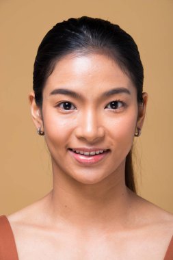 Kuaför makyajı yaptıktan sonra Asyalı kadın. Rötuş yok, sivilceli yeni bir yüz, dudaklar, gözler, yanak, hoş pürüzsüz bir cilt. Stüdyo, estetik terapi için sarı bej hardal arka planını aydınlatıyor.