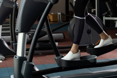 Slim Fitness kadınının beyaz ayakkabıları Fit Gym 'de tırmanma makinesinin eliptik haçı üzerinde ısınıyor. Kavramsal kadın sporcu olabilir. Sağlıklı, kopyalama alanı.
