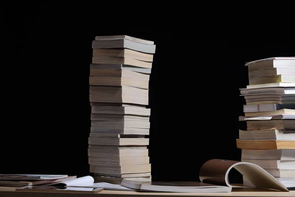 stacking of many kind books, textbooks, journal, report, research, comic in two towers on table with dark black background night time environment