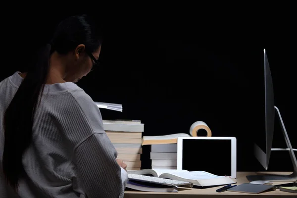 Asian Girl in reading many textbooks on table with many high stacking of international Books and use all device such as tablet, smartphone and computer night time, low exposure, internet of thing