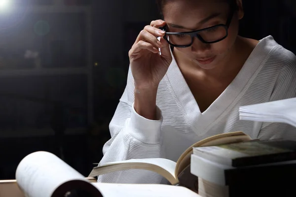 Asian Girl in white shirt reading many textbooks on table with many high stacking of local and international Books Journal Report, Woman works hard during night time, feel asleep tired