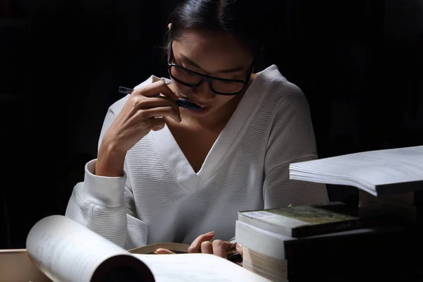 Asian Girl in white shirt reading many textbooks on table with many high stacking of local and international Books Journal Report, Woman works hard during night time, feel asleep tired