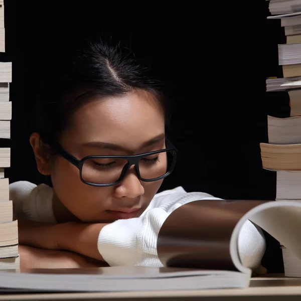 Beautiful Asian Girl open and read magazine between stacking of many kind books, textbooks, journal, report, research, comic in two towers on table night time, she feel asleep, tired, nap and rest