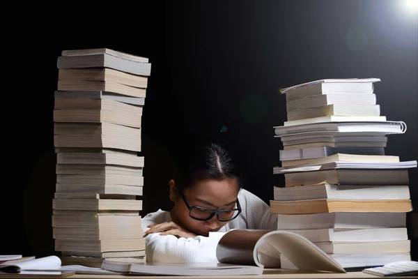 Beautiful Asian Girl open and read magazine between stacking of many kind books, textbooks, journal, report, research, comic in two towers on table night time, she feel asleep, tired, nap and rest