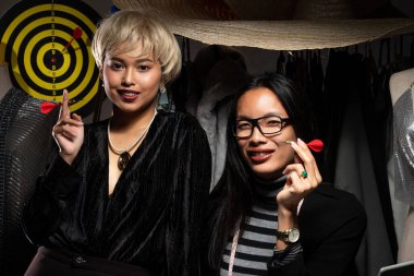 Erkek Fatma İkili sarı saçlar, Ladyboy Siyah Uzun Moda Tasarımcıları Dart 'ı ellerinde tutuyorlar ve kameraya bakıyorlar. LBGT Transseksüel, yeni çevrimiçi mağaza sosyal medya tasarımcısı. Dartboard hedef hedef hedefi