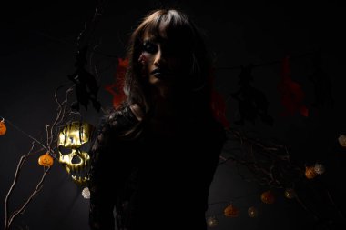 Cadılar Bayramı geçmişinde cadı ve balkabağı çelengi asılı, Yüzünde taze yara olan hayalet zombi kız Yüzünde siyah saç elbisesi korkunç ve tüm perili yerleri öldürmek istiyor