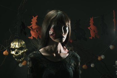 Cadılar Bayramı geçmişinde cadı ve balkabağı çelengi asılı, Yüzünde taze yara olan hayalet zombi kız Yüzünde siyah saç elbisesi korkunç ve tüm perili yerleri öldürmek istiyor