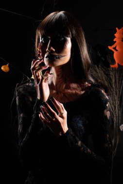 Cadılar Bayramı geçmişinde cadı ve balkabağı çelengi asılı, Yüzünde taze yara olan hayalet zombi kız Yüzünde siyah saç elbisesi korkunç ve tüm perili yerleri öldürmek istiyor