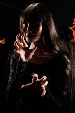 Cadılar Bayramı geçmişinde cadı ve balkabağı çelengi asılı, Yüzünde taze yara olan hayalet zombi kız Yüzünde siyah saç elbisesi korkunç ve tüm perili yerleri öldürmek istiyor