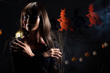 Cadılar Bayramı geçmişinde cadı ve balkabağı çelengi asılı, Yüzünde taze yara olan hayalet zombi kız Yüzünde siyah saç elbisesi korkunç ve tüm perili yerleri öldürmek istiyor