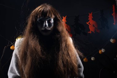 Şeytan beyaz suratlı soytarı siyah kıllı koca ağız Cadılar Bayramı 'nda cadılar ve balkabaklarıyla ayakta duruyor. Ağaç dallarıyla süslenmiş balkabağı kafaları, sade gölgeli fotokopi alanı.