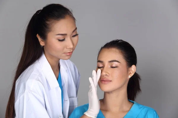 Asian Doctor Nurse check face nose structure before plastic surgery and inject beauty chemical syringe to patient, Studio lighting grey background