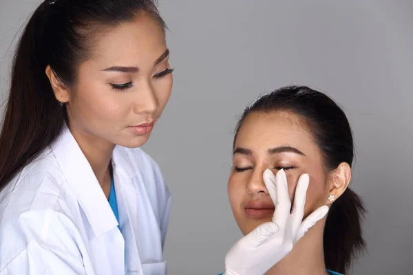 Asian Doctor Nurse check face nose structure before plastic surgery and inject beauty chemical syringe to patient, Studio lighting grey background