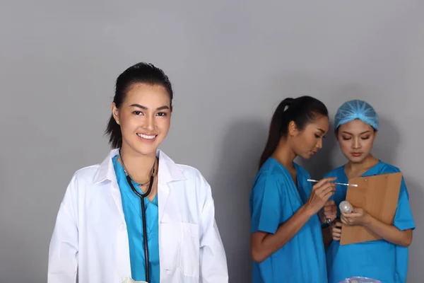 Beautiful Asian Woman Doctor in white shirt stethoscope and two Nurses chart hygine hat talking blur, Studio lighting grey background