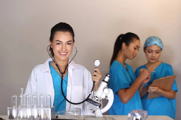 Beautiful Asian Woman Doctor in white shirt stethoscope show syringe and two Nurses chart hygine hat talking blur, Studio lighting grey background