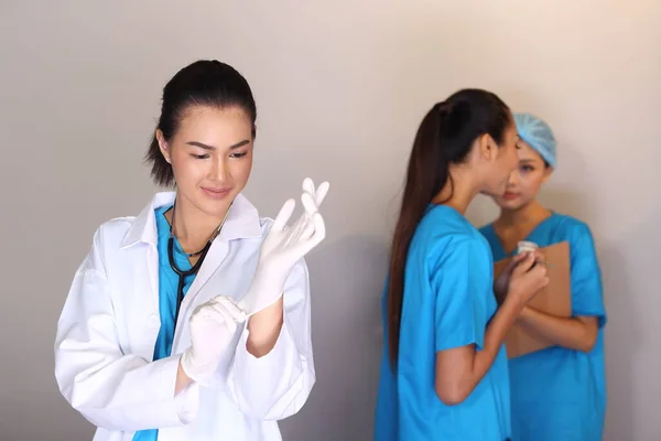 Beautiful Asian Woman Doctor in white shirt stethoscope show Rubber gloves and two Nurses chart hygine hat talking blur, Studio lighting grey background