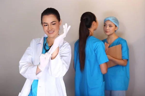Beautiful Asian Woman Doctor in white shirt stethoscope show Rubber gloves and two Nurses chart hygine hat talking blur, Studio lighting grey background