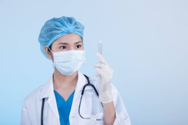 Steteskoplu, lastik eldivenli, şırıngalı, koruyucu maskeli, tıp hastanesinde hijyen şapkalı, yarı siyah saçlı, portresi siyah, mavi arka plan fotokopi alanı olan Asyalı güzel doktor hemşire kadın.