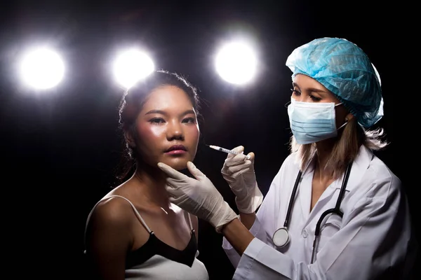 Caucasian Doctor Nurse woman in uniform with stethoscope, check jawline bone face of asian girl before plastic surgery treatment injection, studio lighting four back light flare silhouette copy space