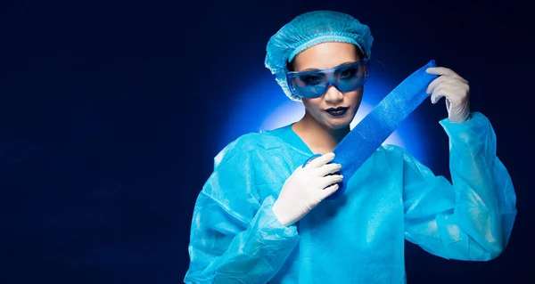 Luxury Asian Beautiful Doctor Nurse woman in uniform with Hygiene cap, gloves, glasses hold special blue bandage in Medical hospital, portrait, studio lighting gradient blue background copy space
